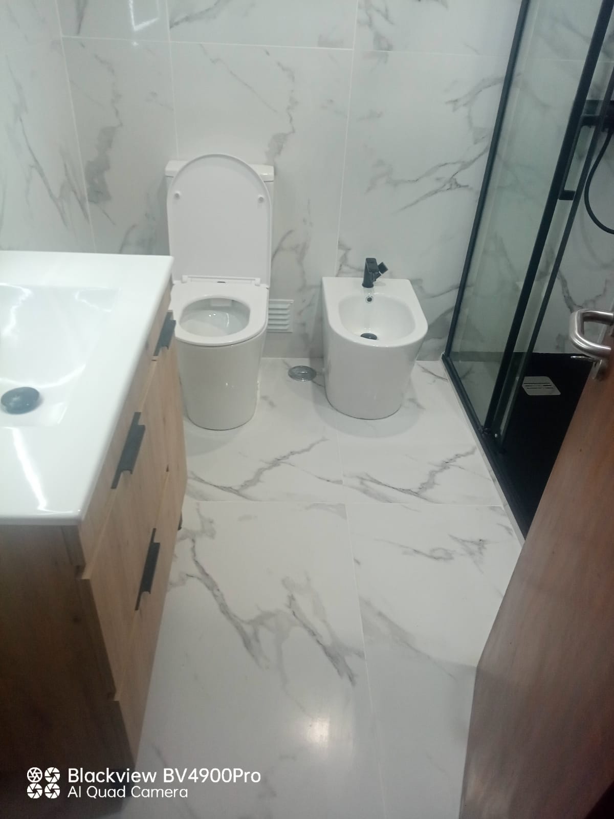 Casa de banho moderna em mármore branco, sanita e bidé suspensos com duche de vidro preto — projecto Pontes e Periferias em Lisboa